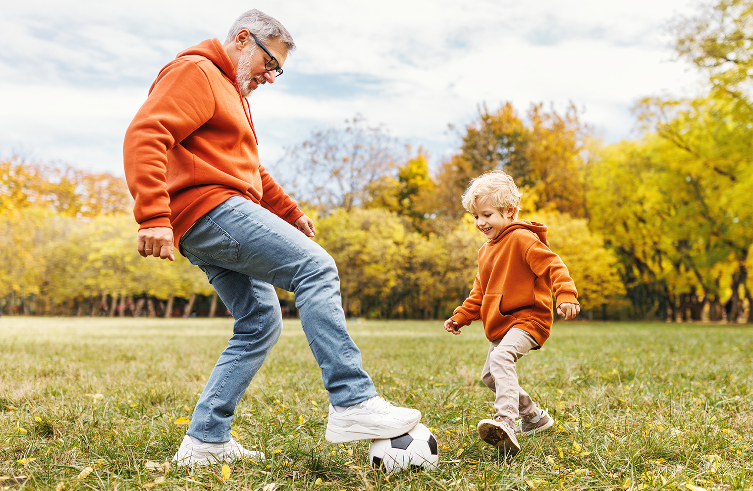 A man and his son playing with a soccer ball in a grassy field