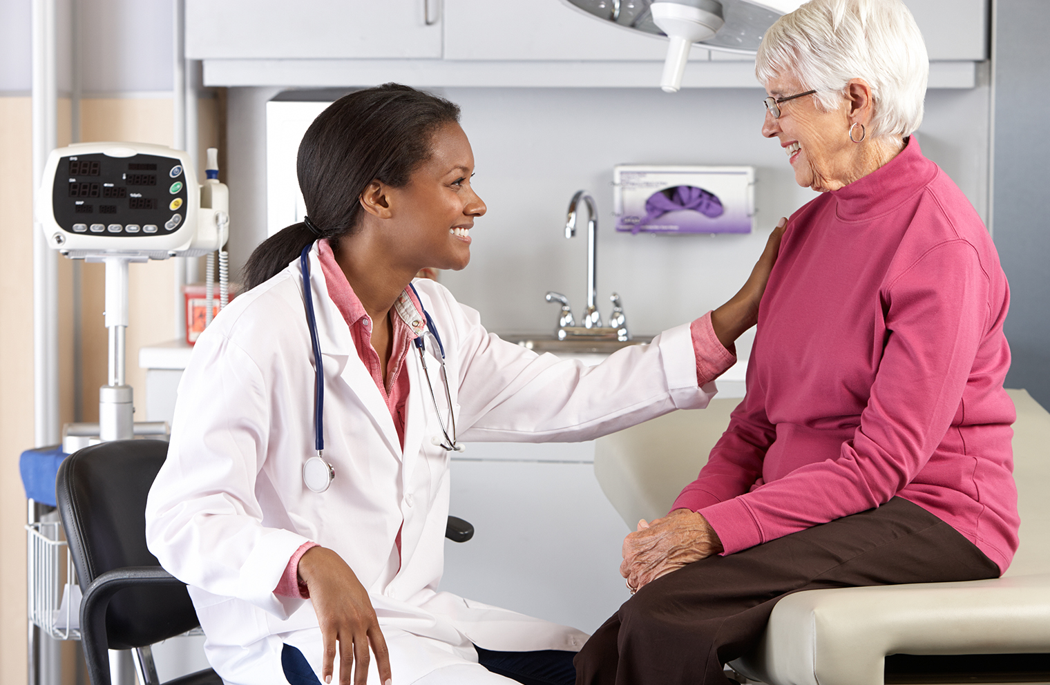 A health care provider smiles at her patient as they discuss health insurance in an exam room.
