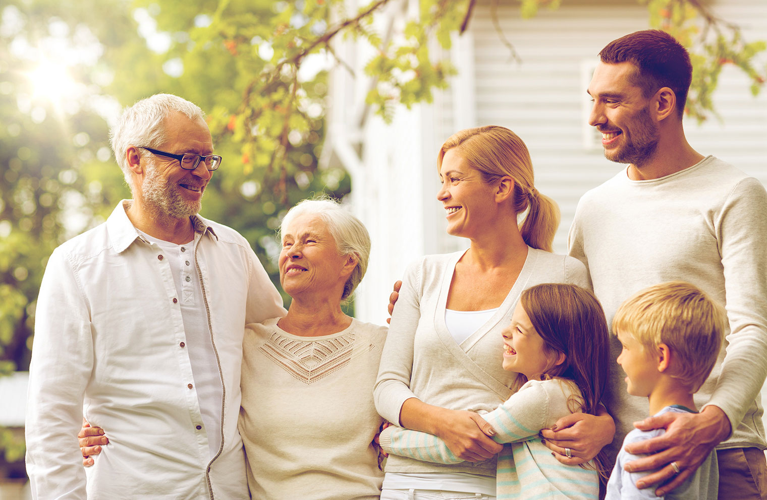 Grandparents, children and grandchildren hug and smile in front of a home.