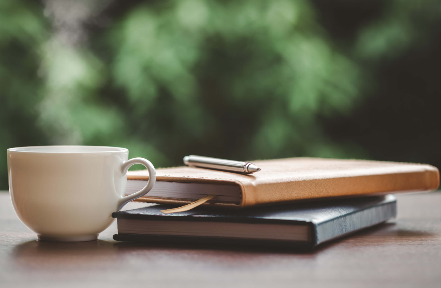 coffee mug on table next to two journals and pen