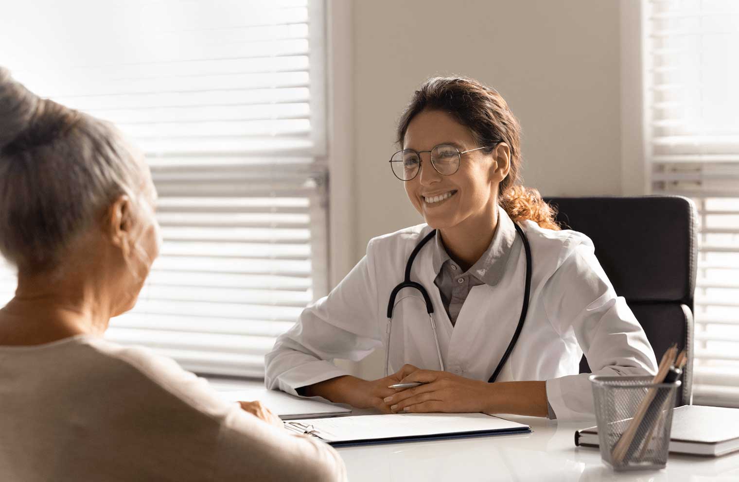A health care professional smiles at her patient as they sit at a desk together.