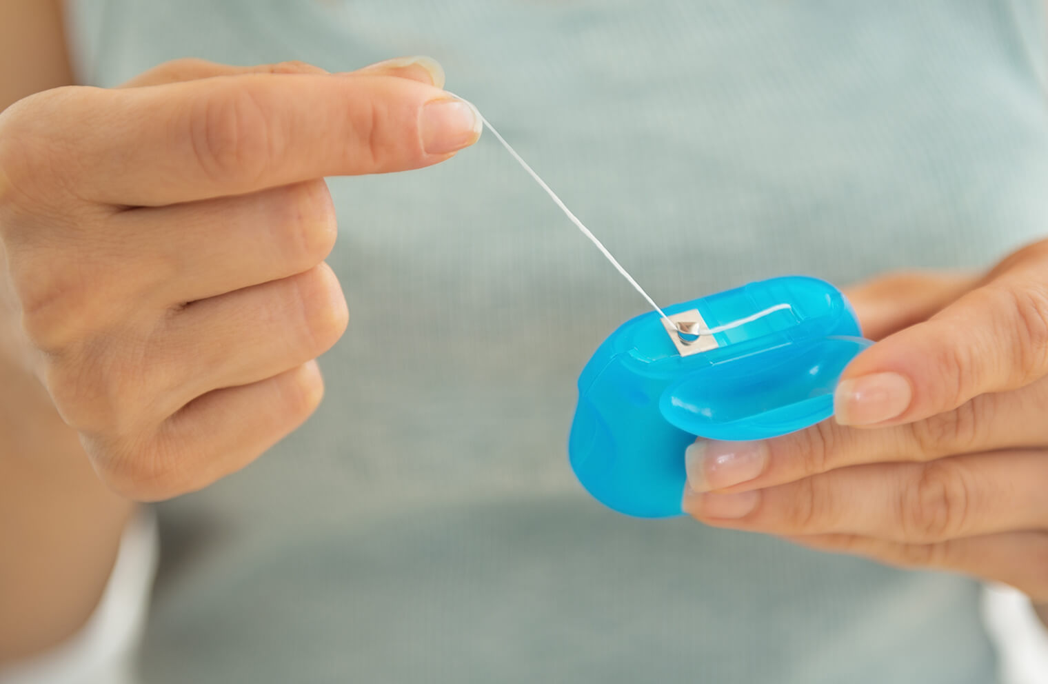 Close up picture of a woman's hands pulling floss out of a blue container.