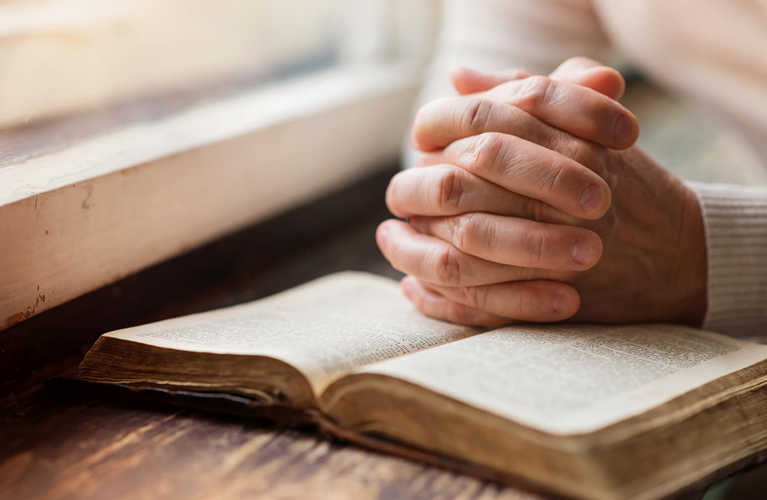 Close up picture of hands clasped together in prayer on top of a bible.