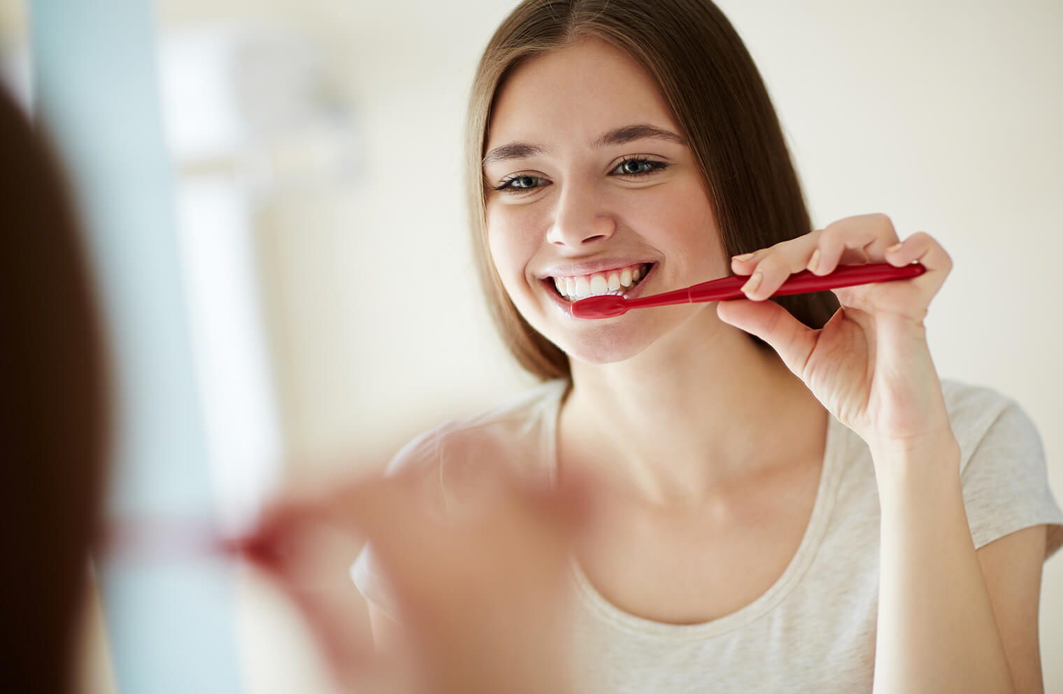 A woman smiles as she looks in the mirror to brush her teeth. 