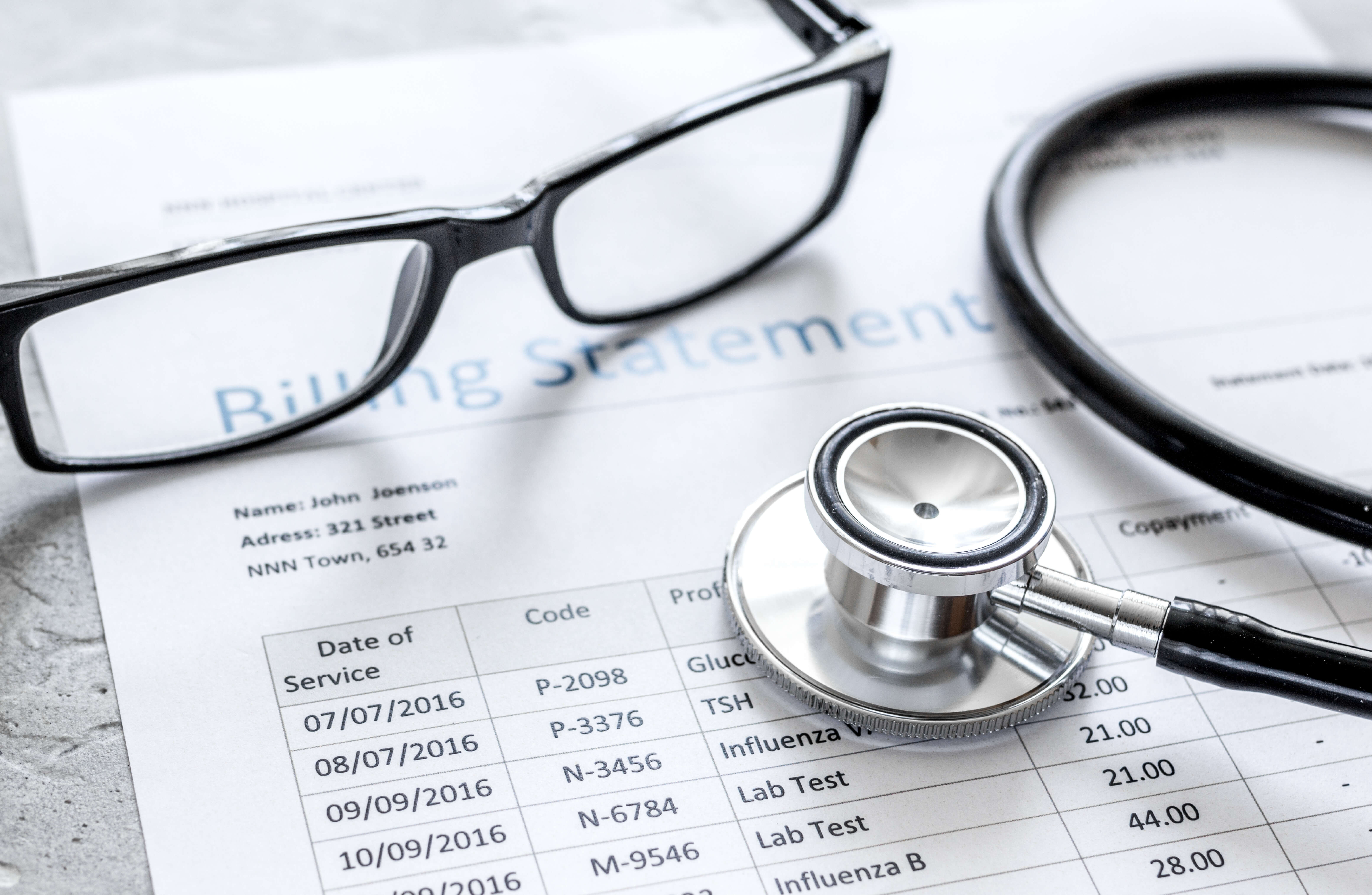stethoscope with eye glasses on top of medical bills