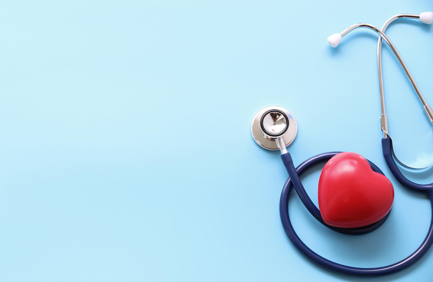 Picture of a stethoscope wrapped around a heart-shaped squishy toy on a blue background.