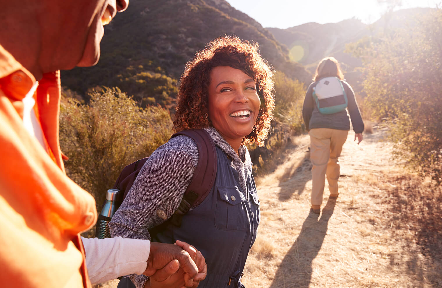 A man and woman smile and hold hands as they hike on a trail.
