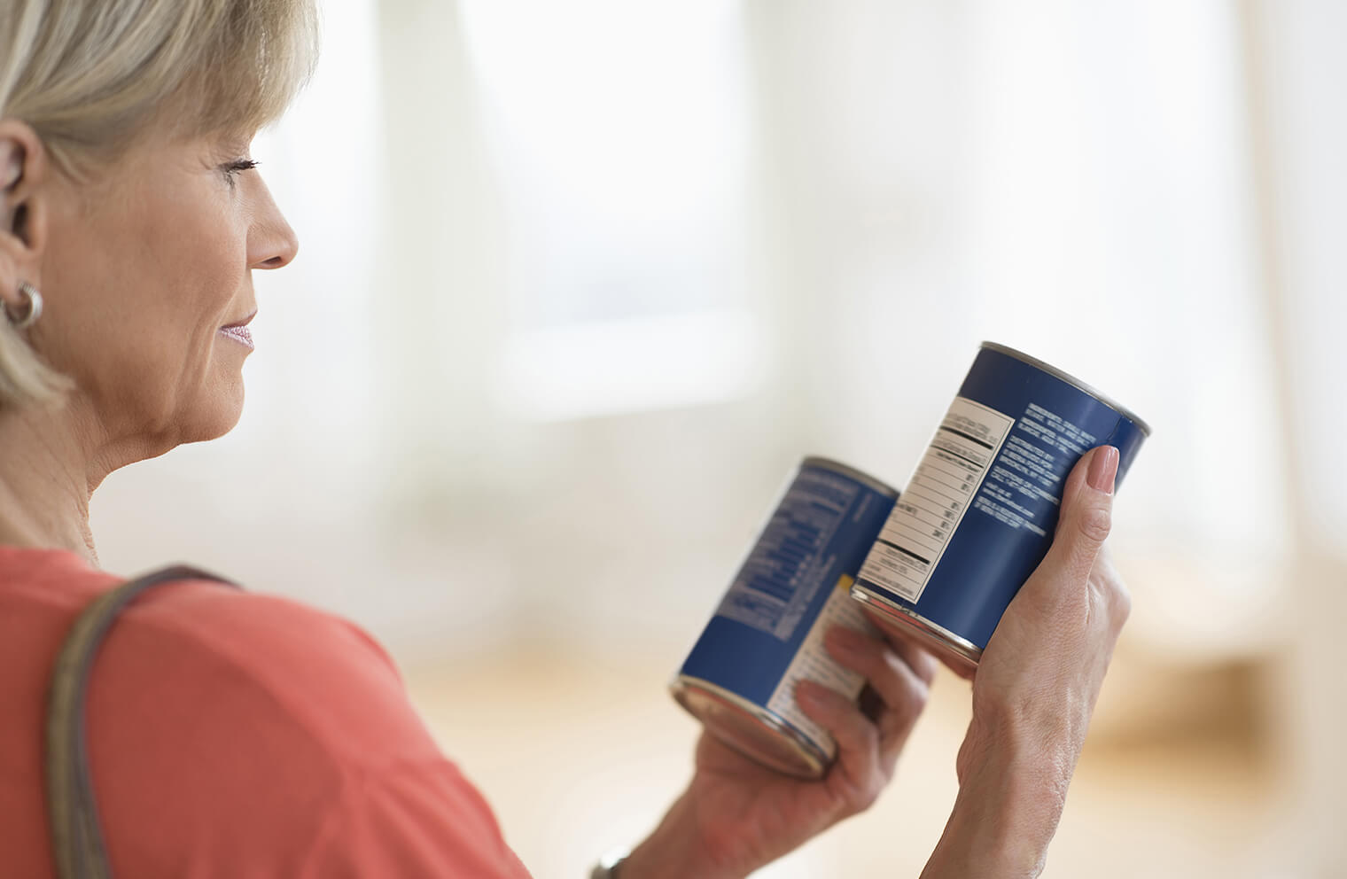 Picture of a woman reading the nutritional information on two different cans of food.