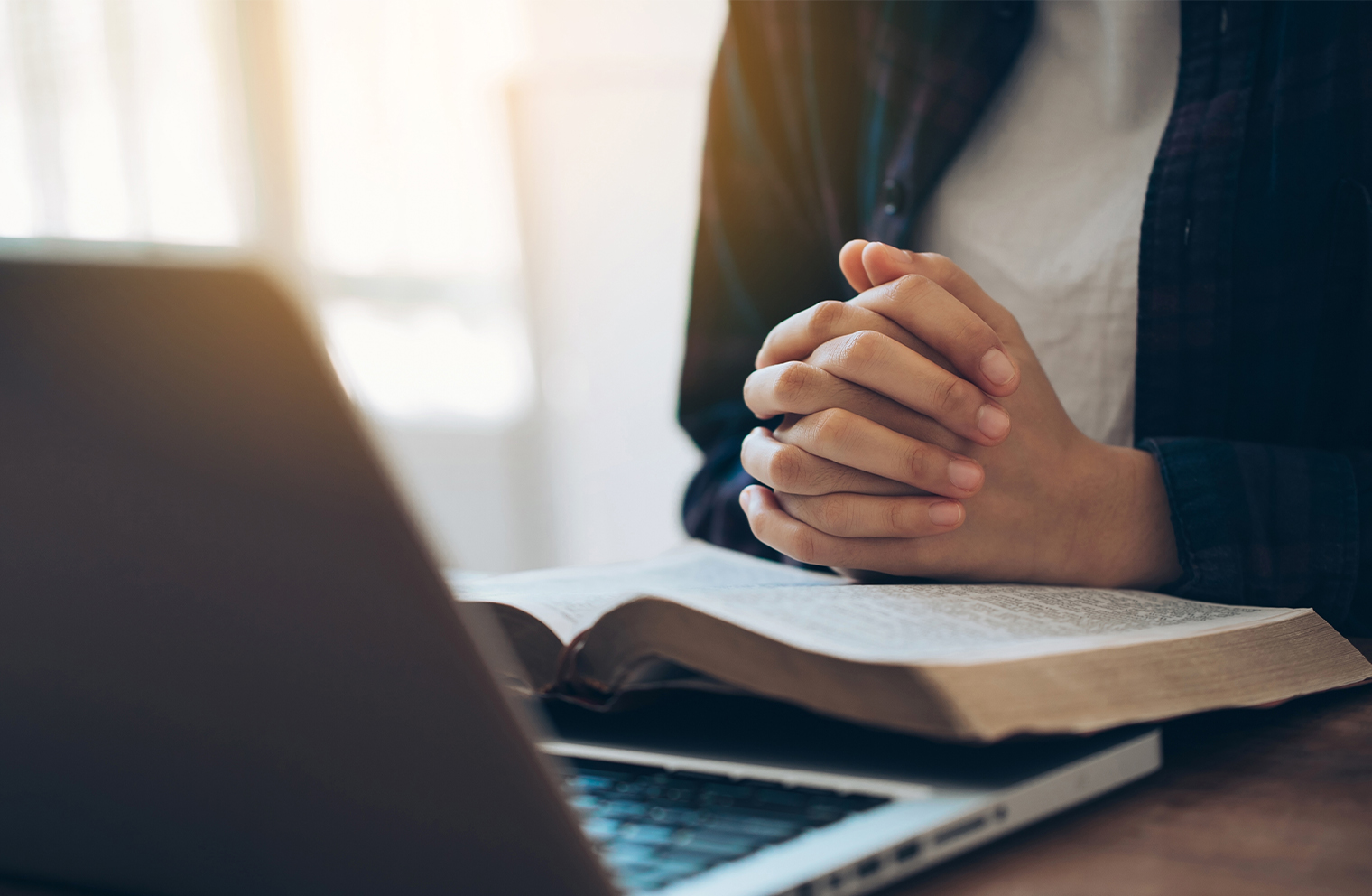 A person with an open Bible in front of a laptop used for Christian investing.