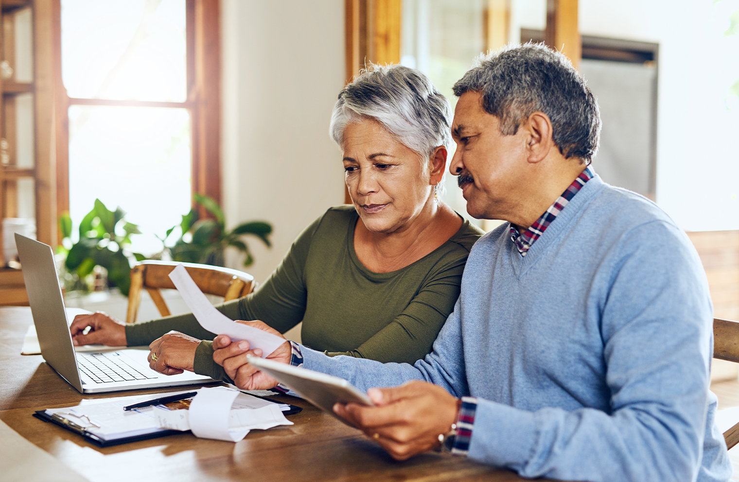 An older man and woman looking at receipts with a laptop nearby