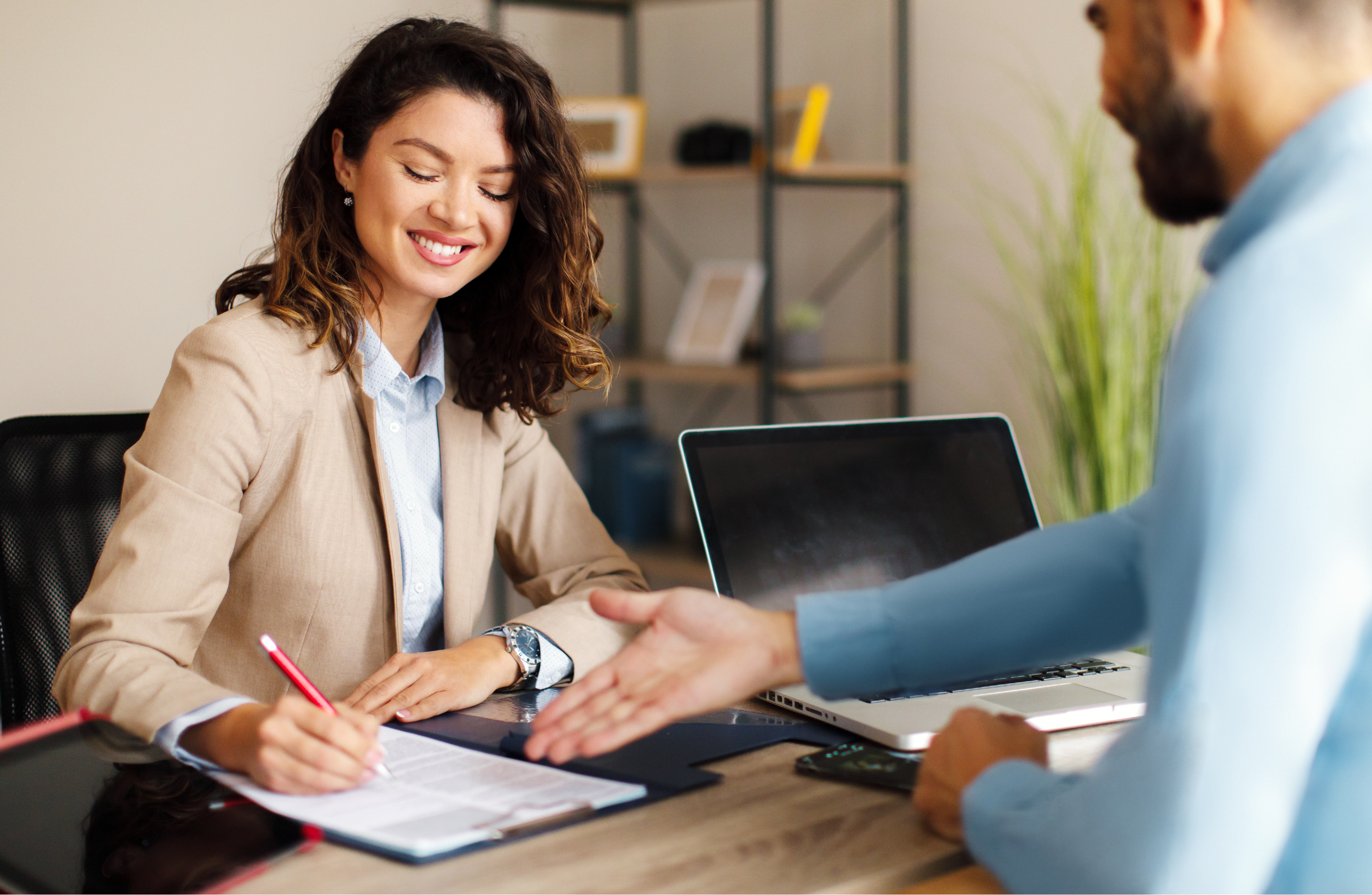 A woman completes onboarding paperwork at a desk with a manager. 