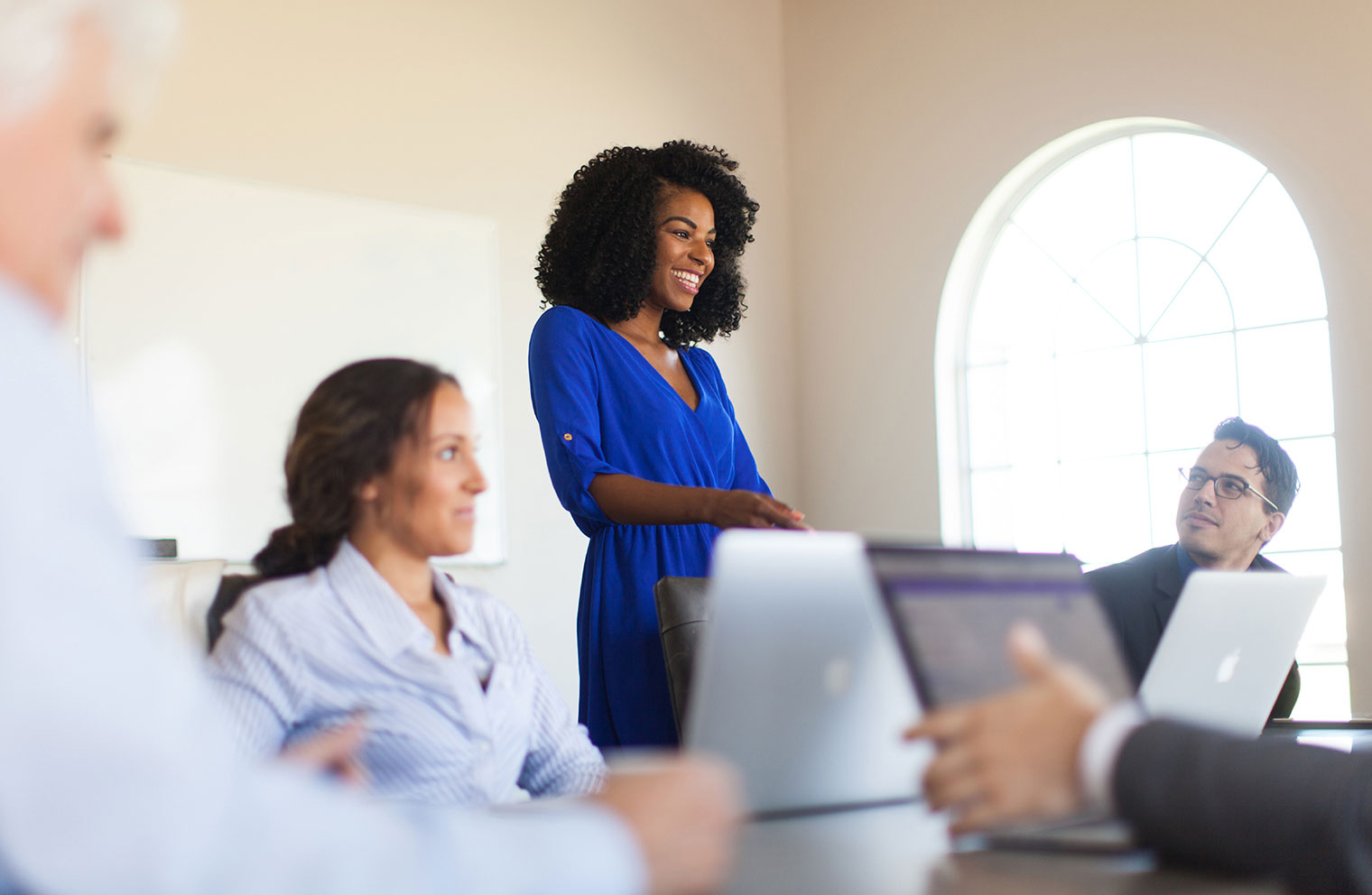 A woman gives a presentation to a group of colleagues in an office setting.