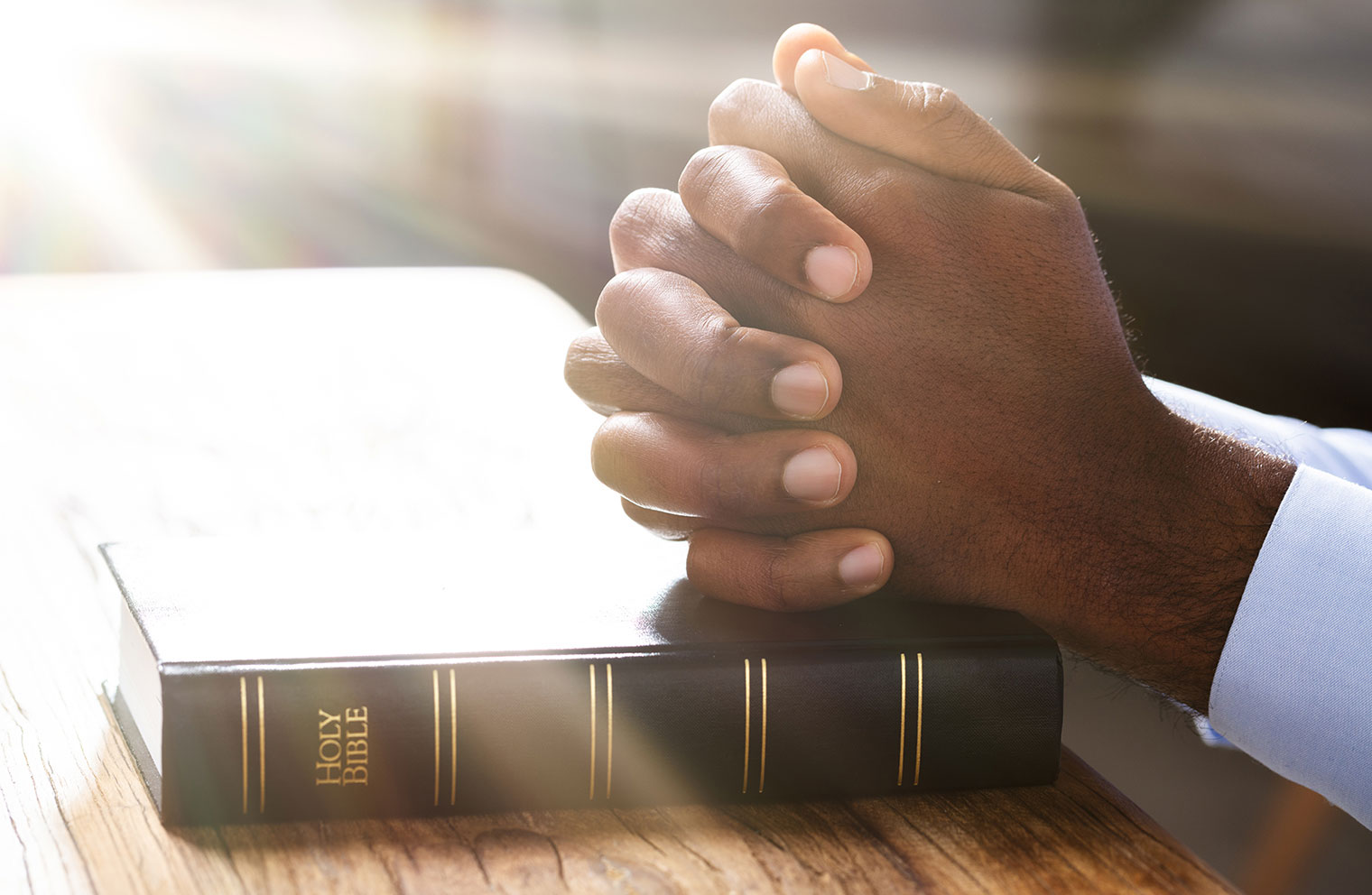 Folded hands rest on a Bible. 