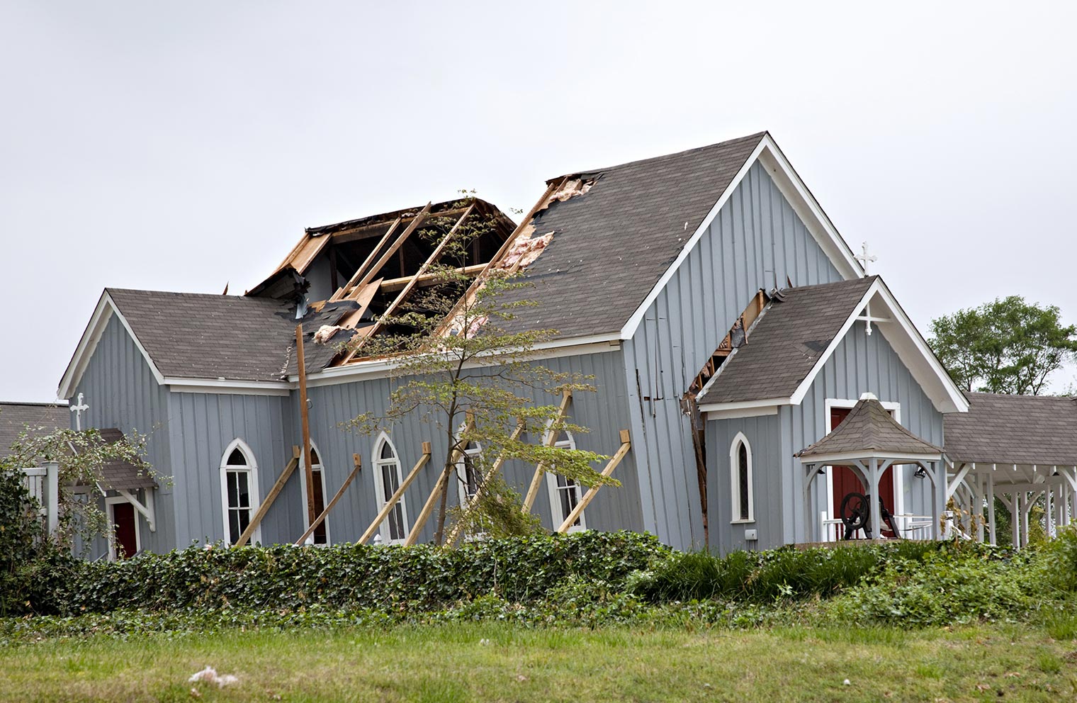 Part of the roof is missing from a damaged church, which is leaning to one side and being upheld by beams. 