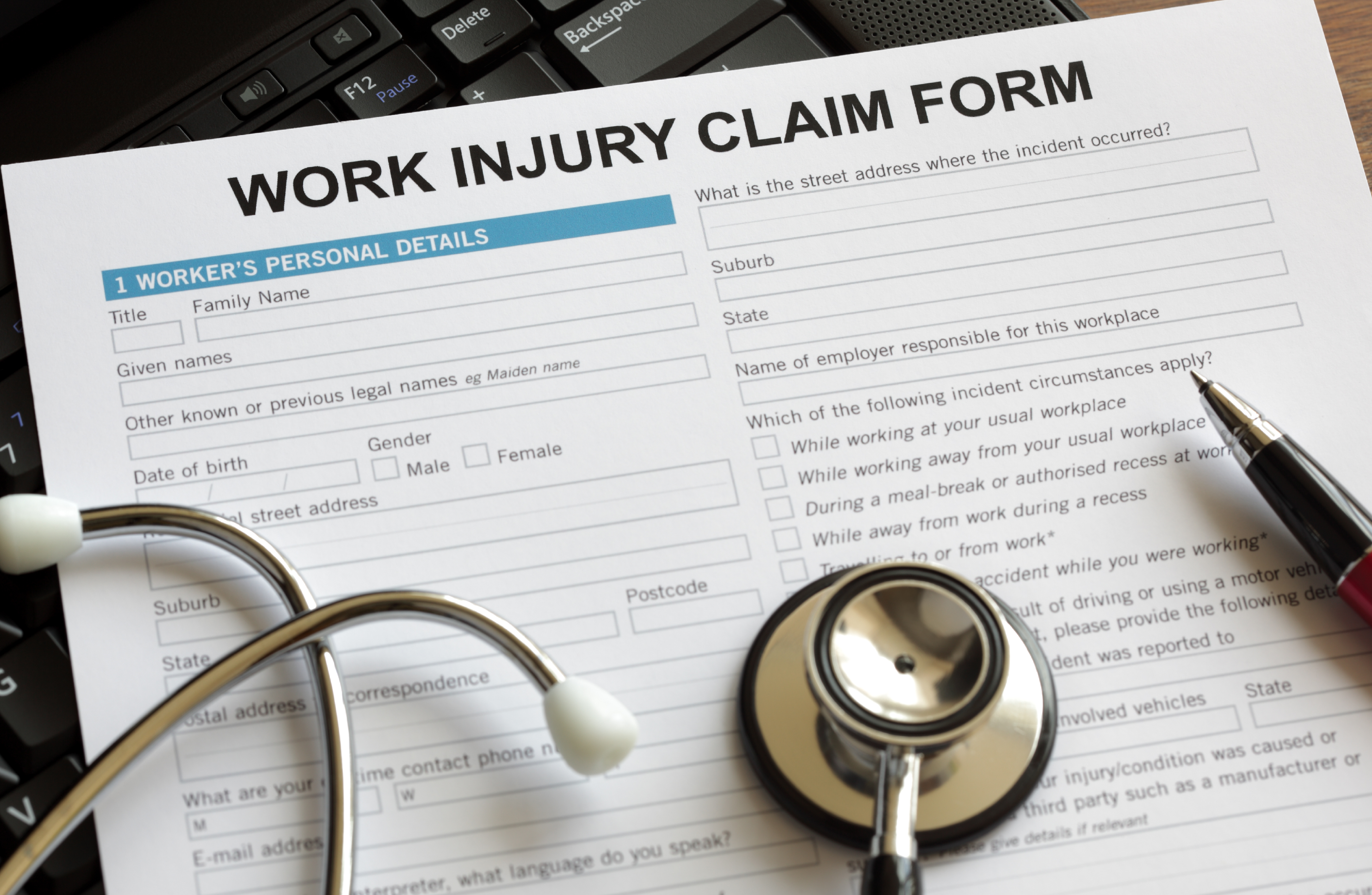A stethoscope and pen on top of a work injury claim form.