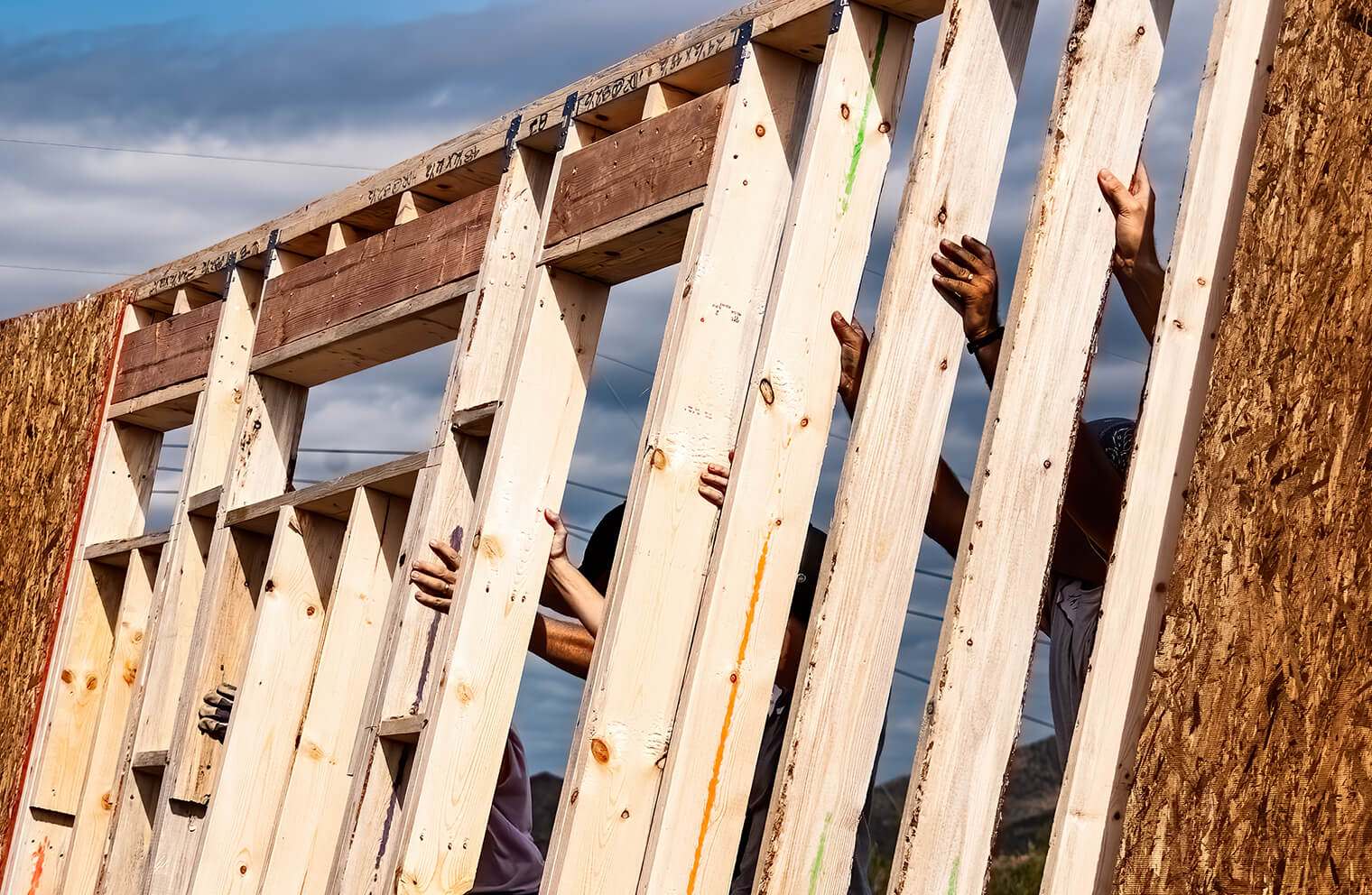 Picture of people putting up wooden framing for a wall. New construction and repair.