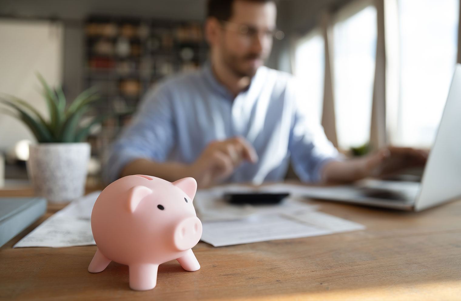 Picture of piggy bank with man calculating expenses in background