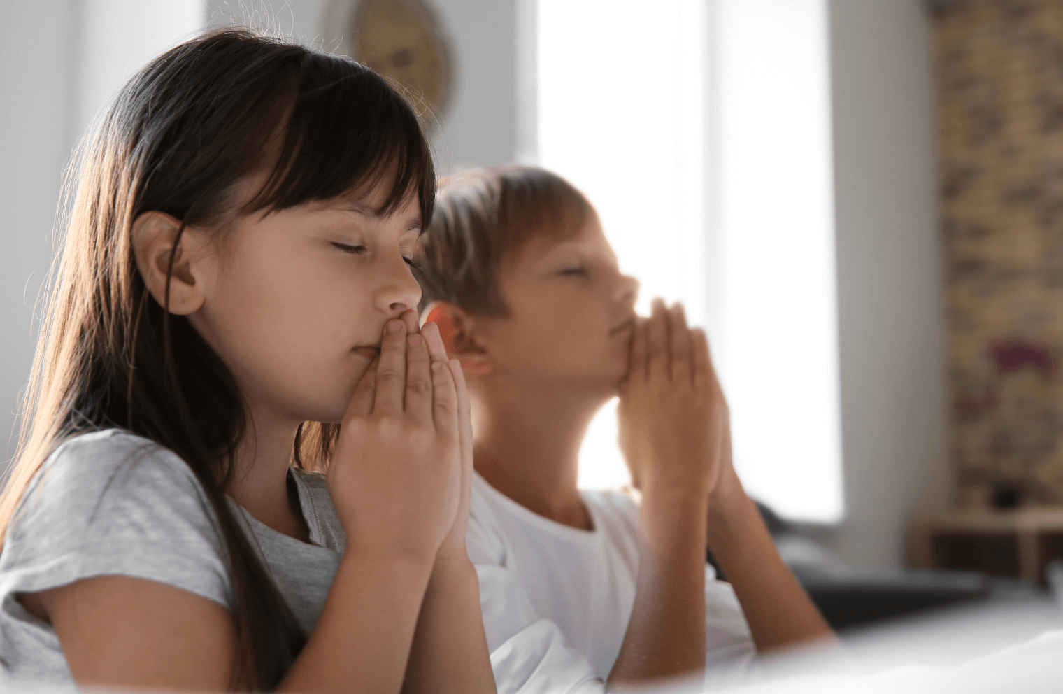 Two children inside a church pray with folded hands.