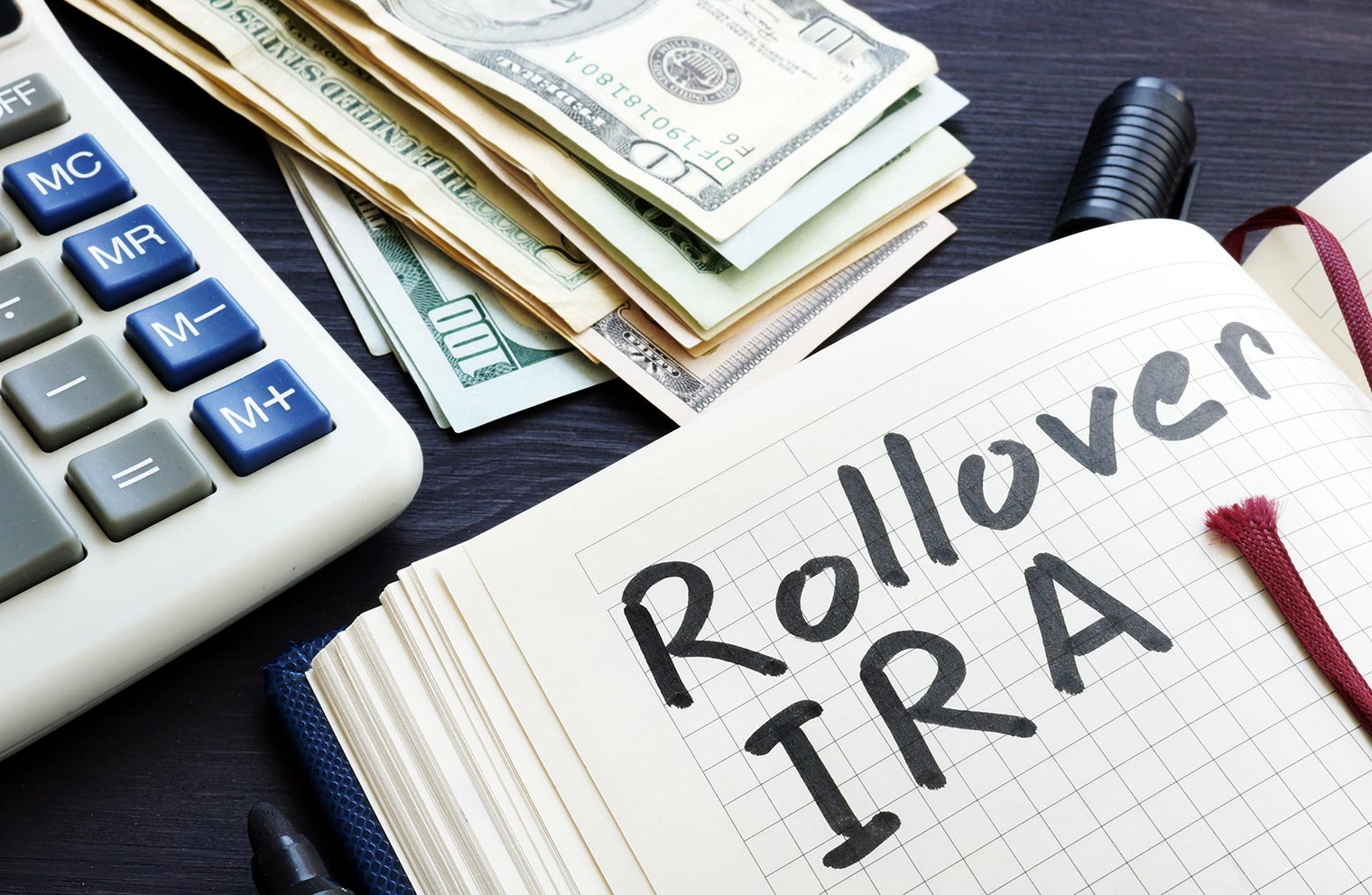 Image of tabletop with notepad, calculator, and dollar bills.