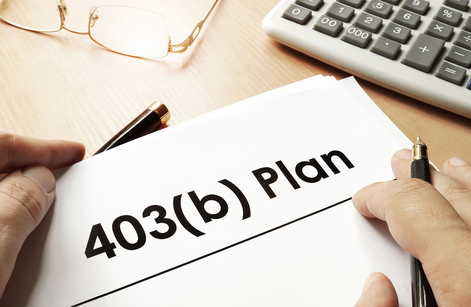 Hands holding a 403(b) retirement plan document beside a calculator and eyeglasses.