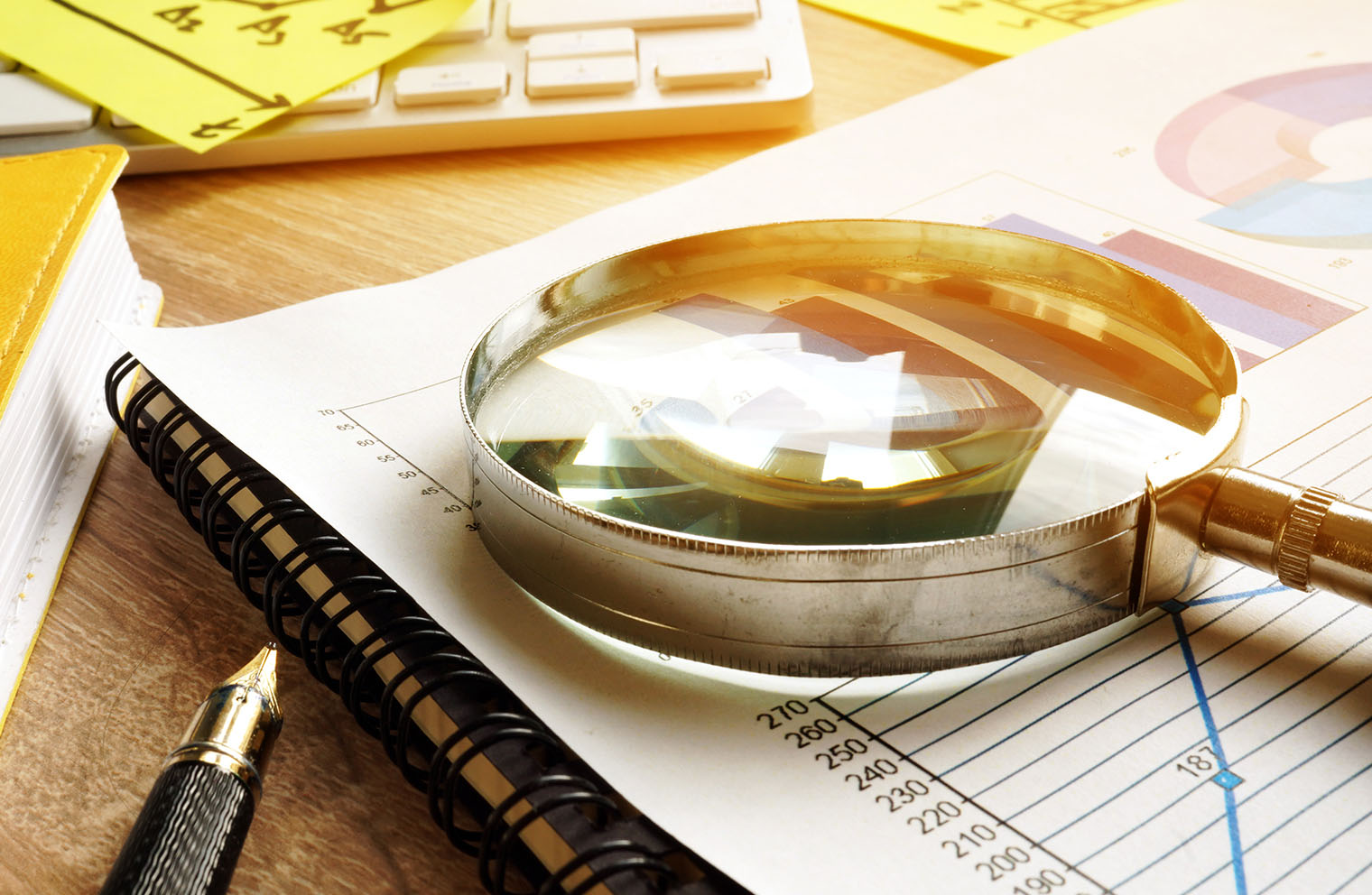Image of magnifying glass  on top of paper with charts and other office paraphernalia