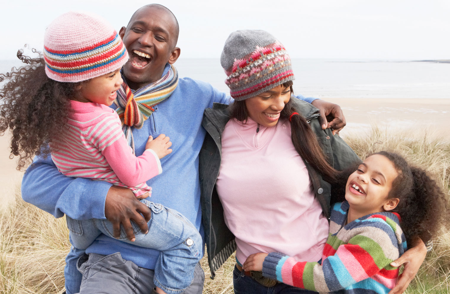Picture of husband and wife with two daughters, laughing in a field.