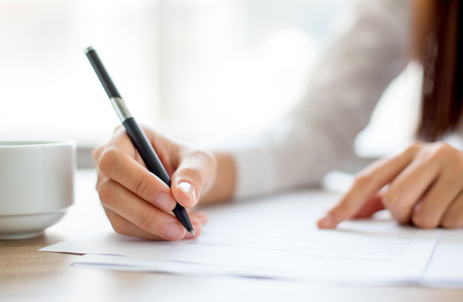 Image of woman at desk with pen and documents.