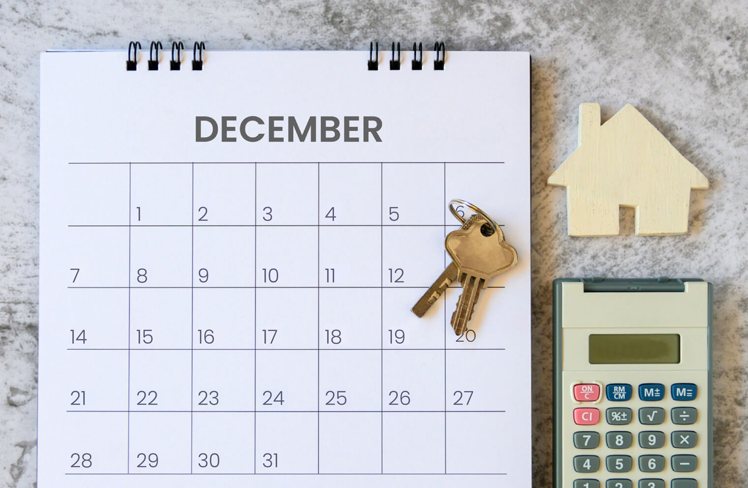 Picture of a calendar with the month of December showing. There are a set of house keys on top of it and a calculator next to it.