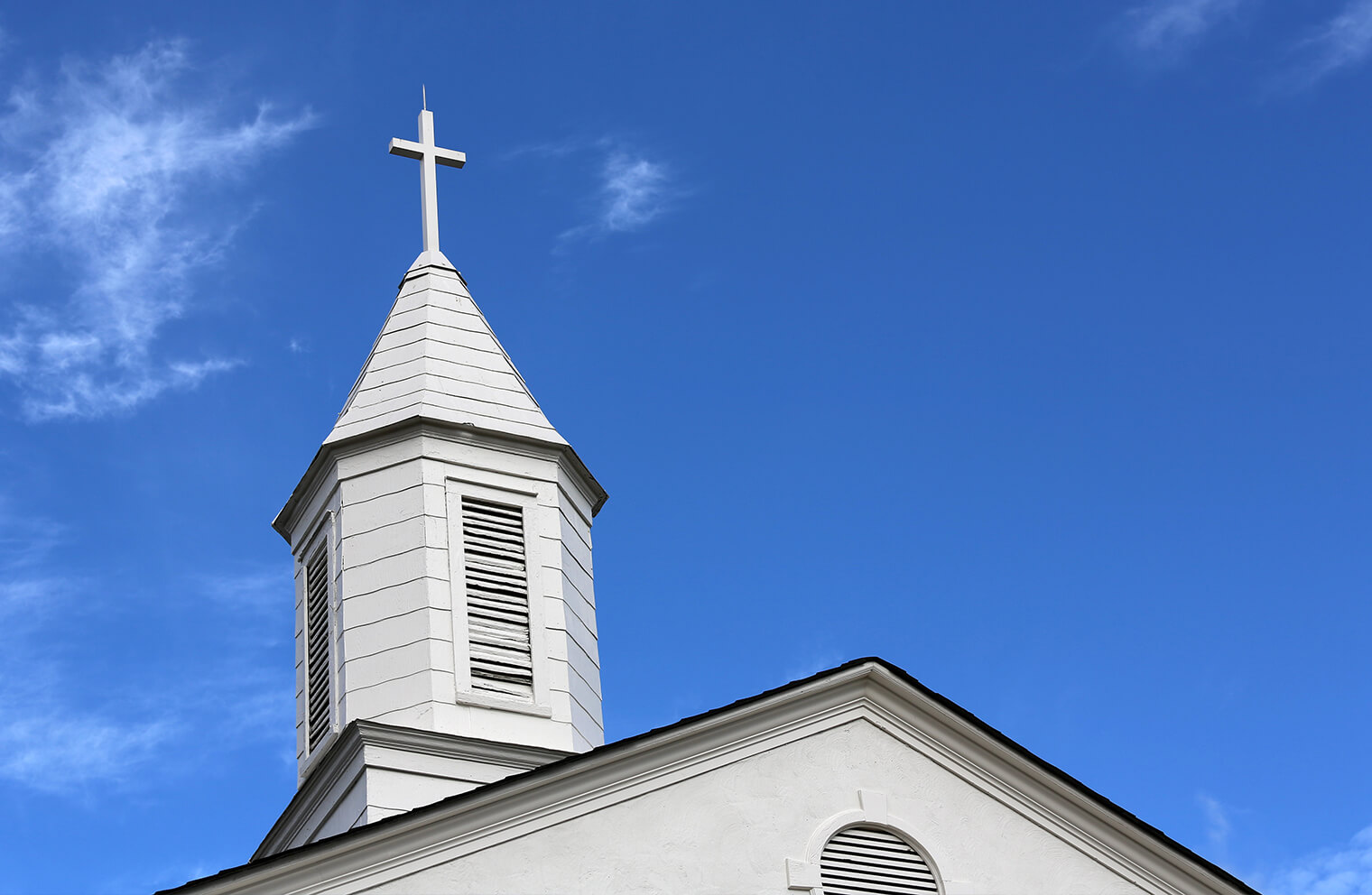 Image of a white wooden steeple with a blue sky in the background.