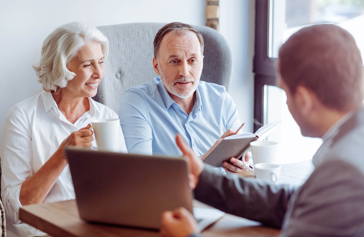 An older man and woman sitting across the table from a man with a laptop