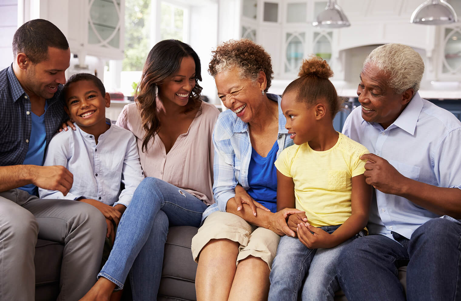 Picture of a multi-generational family sitting together on a gray couch with a white kitchen in the background.
