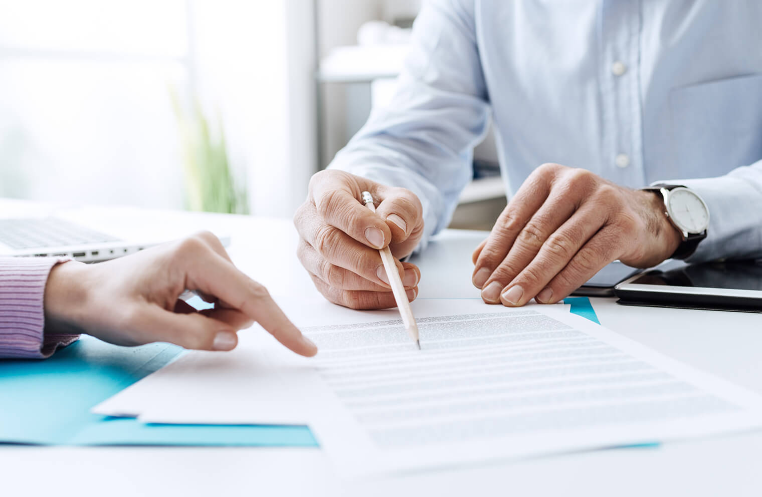 Close up picture of a man's hands holding a pencil that is on a document. There is also a woman's hand pointing at the same document.
