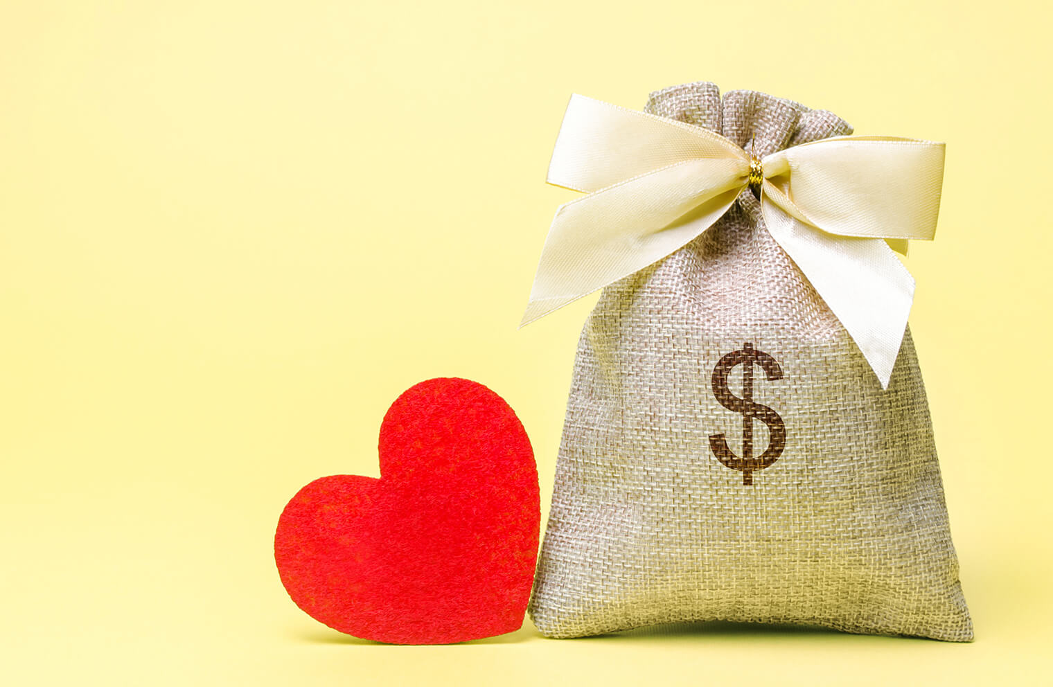Image of a felt heart next to a burlap sack with dollar sign on it and a yellow background.