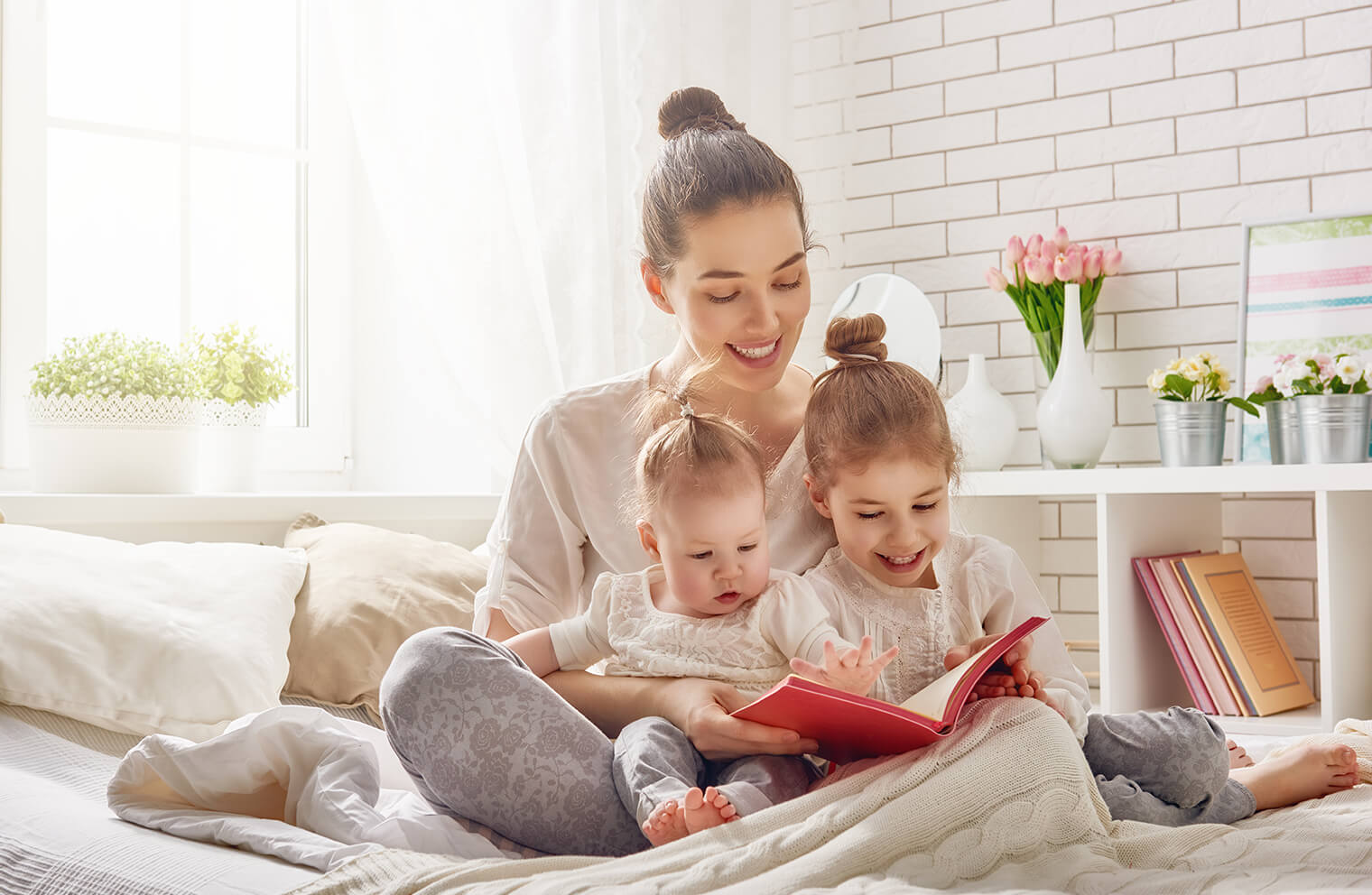 Picture of mother and young kids reading a book together on a bed.