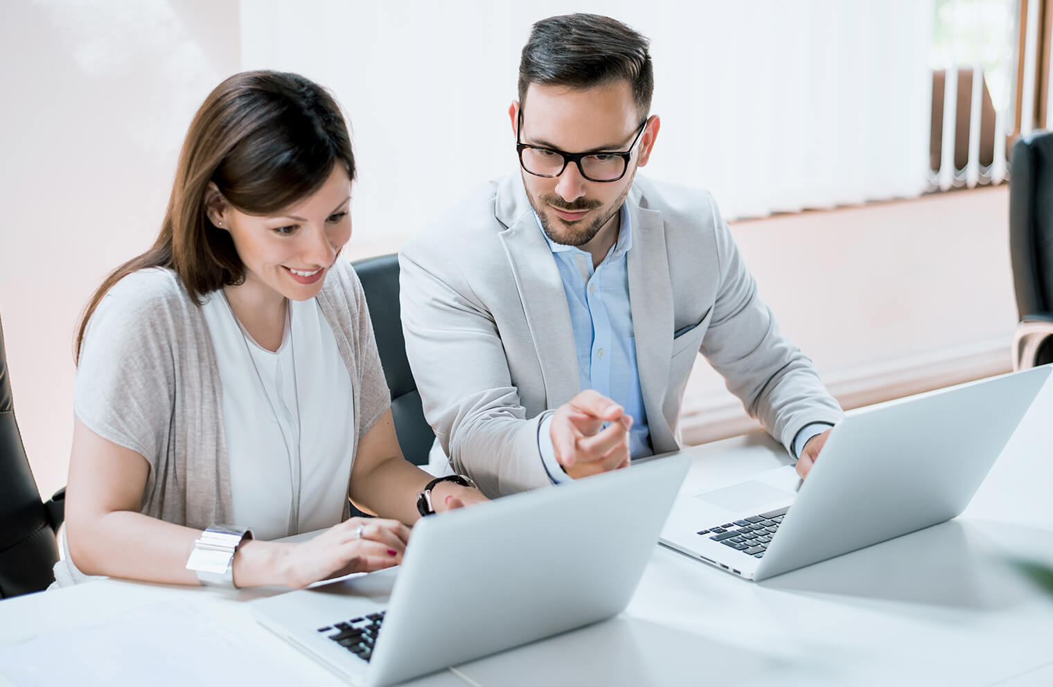 Picture of a woman and man sitting at a desk together working on their laptops.