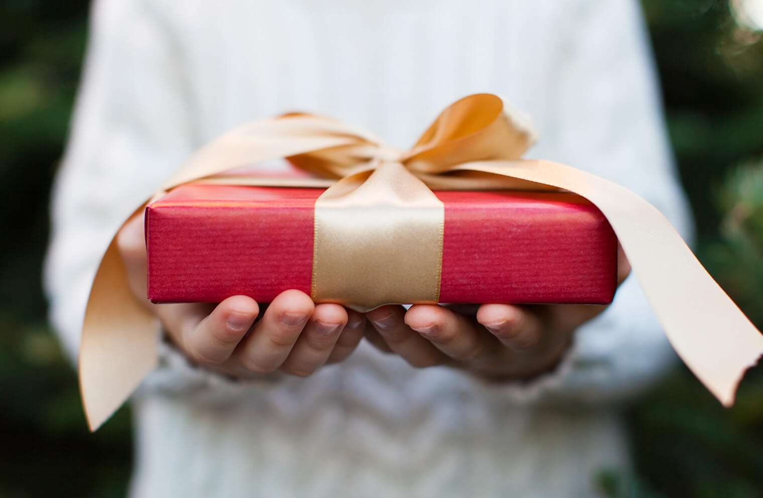 Close up picture of a person holding a red gift with a golden ribbon.