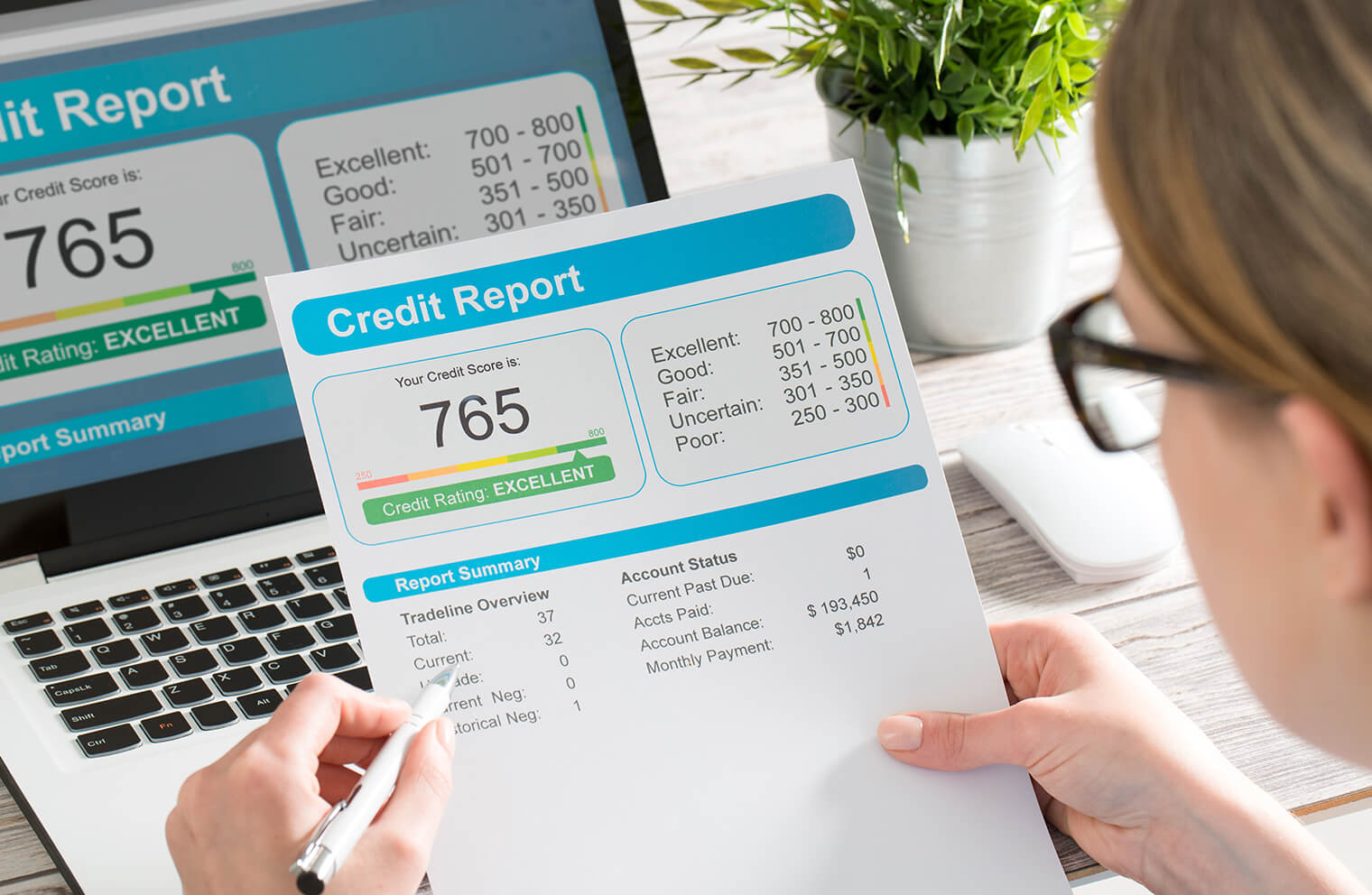 Picture of a woman in glasses reviewing her credit report on a paper and on a laptop.