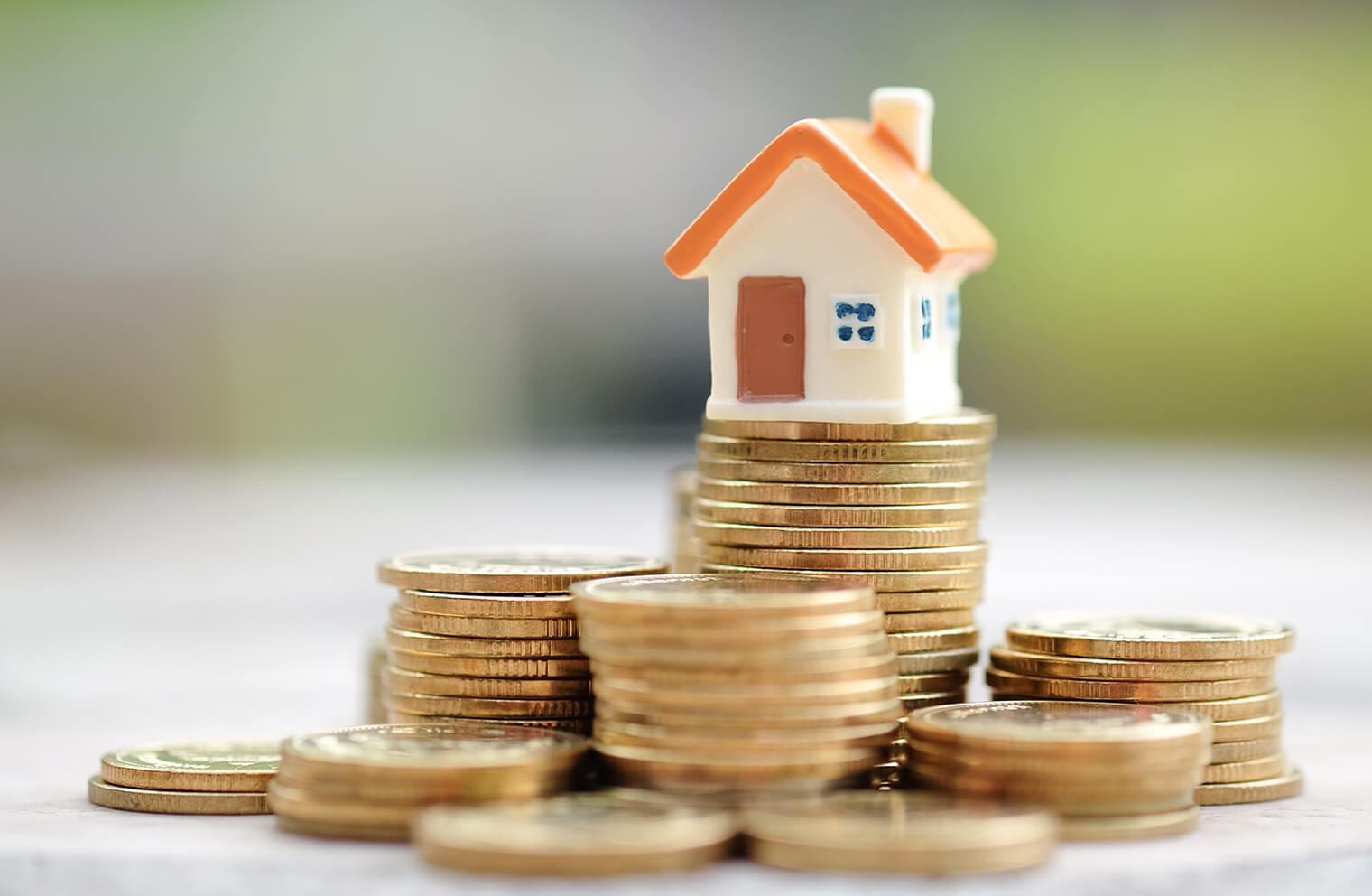 Close up image of a tiny toy house sitting on top of a stack of coins.