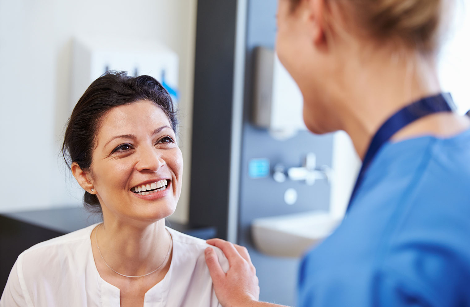 Image of woman smiling as she receives checkup from female doctor.